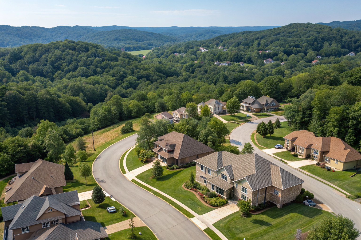 Aerial view of homes with shingle roofs along curving streets among wooded ridges