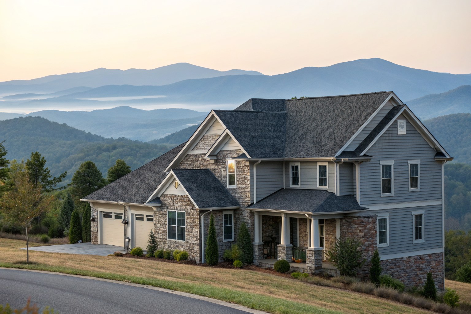 A two-story stone and siding home with a dark shingle roof on a hillside, with blue mountain ridges behind